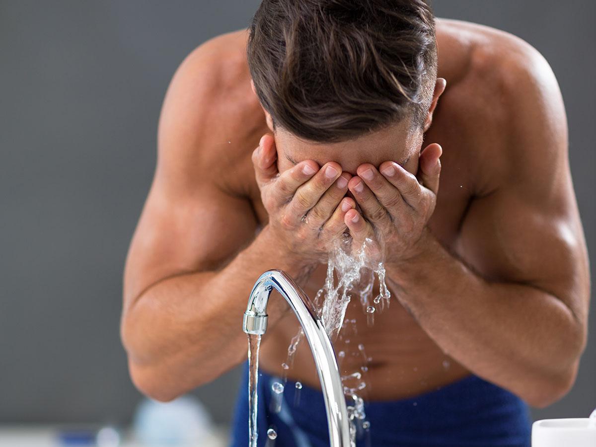 Man washing his face in the sink with water.